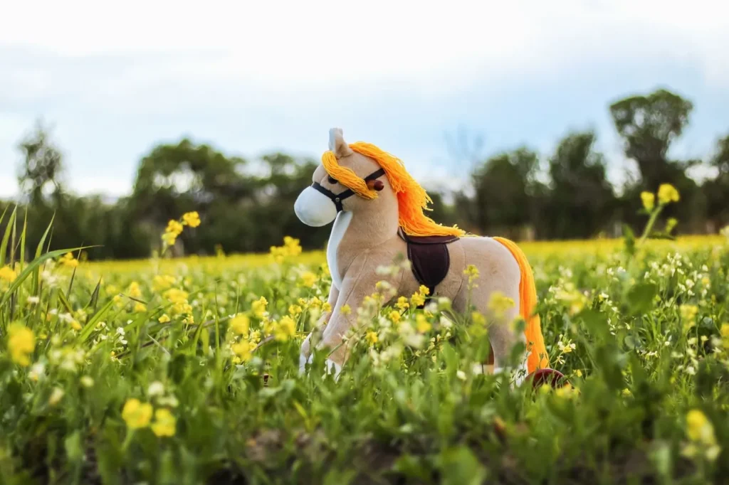 Plyshest med blød tekstiloverflade og orange manke af kunstpels står i en blomstrende grøn mark